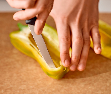 Hände schneiden eine gelbe Paprika mit einem Messer auf einem Schneidebrett.