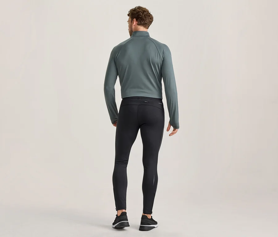 Mann von hinten, trägt ein dunkelgrau-türkises, langärmeliges Sportoberteil mit Reißverschluss, schwarze eng anliegende Laufleggings mit reflektierenden Details und schwarz-weiße Sportschuhe.