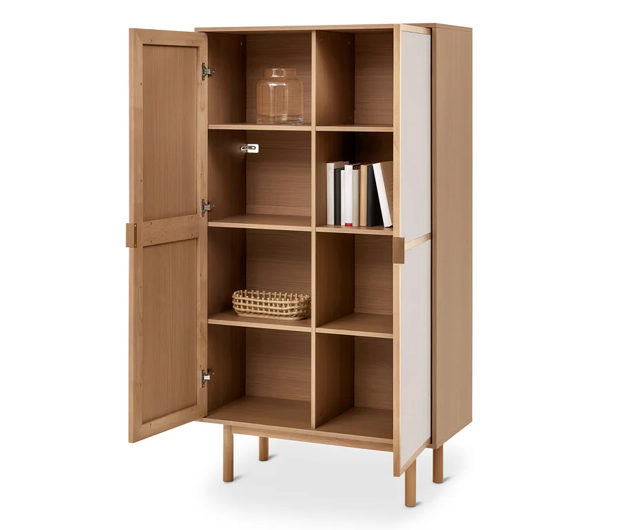 Heller Holzschrank mit offener Tür links, die Regale zeigt. Darin sind ein Glasgefäß, Bücher und ein geflochtener Korb sichtbar. Die rechte Seite hat weiße Paneele.