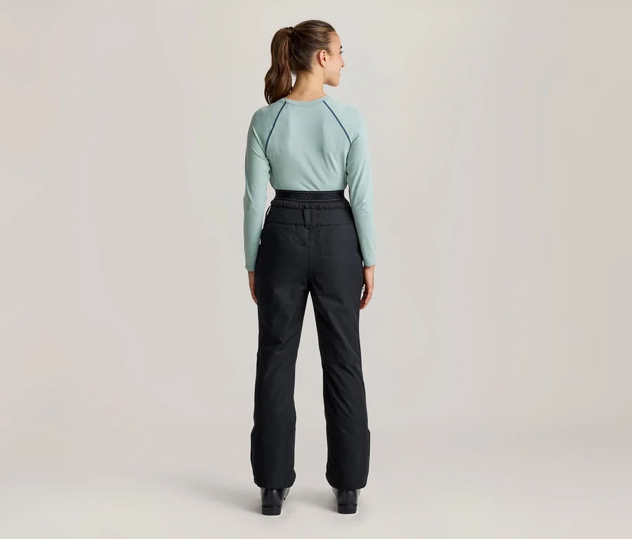 Frau von hinten, die ein hellblaues Langarmshirt und eine schwarze Skihose trägt. Ihr Haar ist zu einem Pferdeschwanz gebunden.