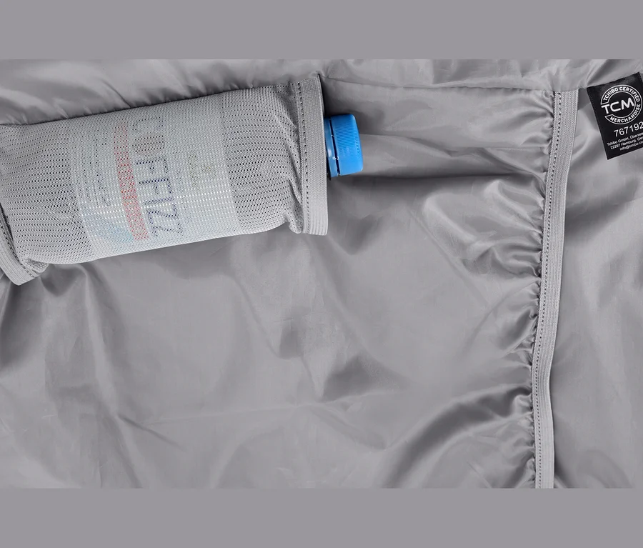 Graues Gewebe mit einer Netztasche, die eine Flasche mit blauem Verschluss und der Aufschrift „COFFEEZZ“ enthält. Rechts ist ein TCM-Etikett zu sehen.