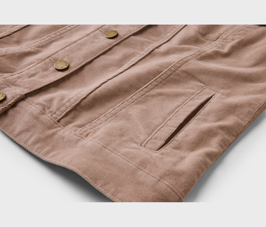 Nahaufnahme einer hellbraunen Cordjacke, die ihre gerippte Textur, goldfarbene Knöpfe und eine seitliche Eingrifftasche zeigt.