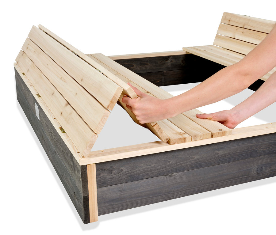 Eine Frau montiert den EXIT XL-Sandkasten »Aksent« aus dunklem Holz mit hellen Holzlamellen.