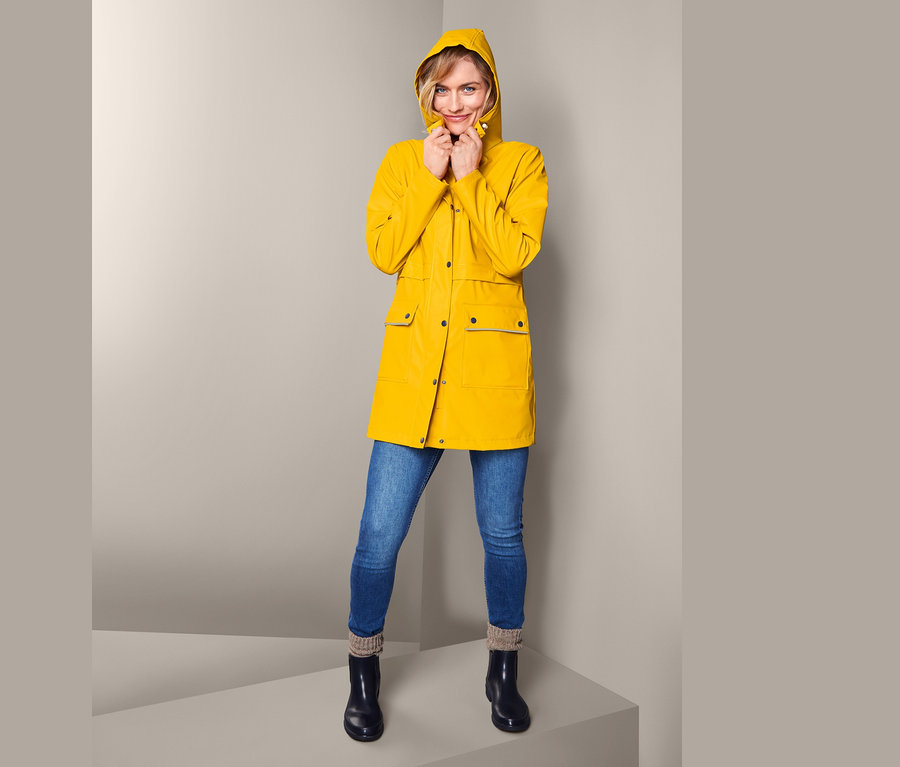 Frau trägt einen gelben Regenparka »Friesennerz«, blaue Jeans und schwarze Stiefel.
