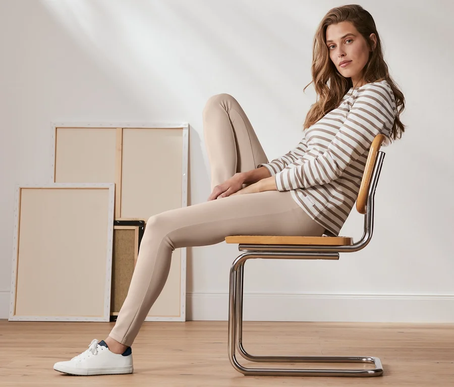 Frau sitzt auf Stuhl, trägt eine geringelte Bluse und eine Basic-Leggings aus Heavy-Jersey in Creme.