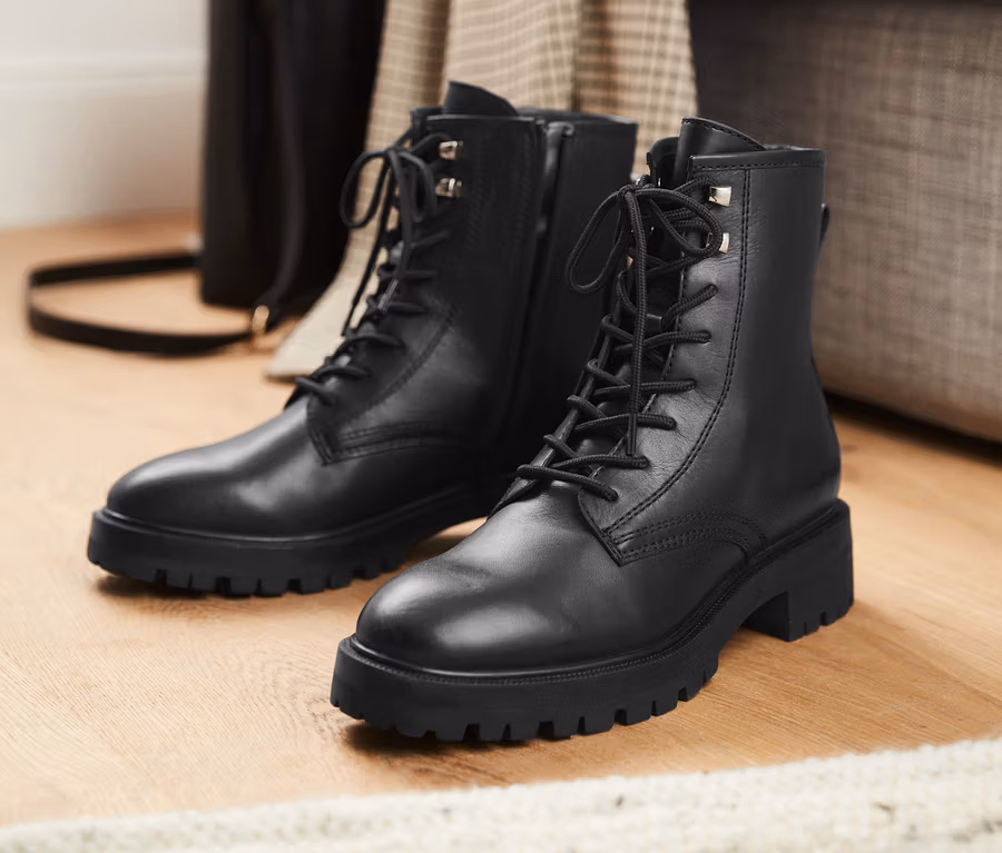 Schwarze Leder-Boots stehen auf einem Holzboden.