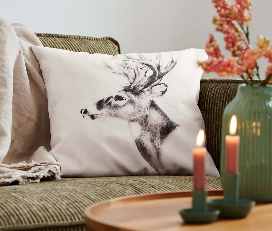 Ein Dekokissen-Bezug mit Hirschmotiv liegt auf einem Sofa.