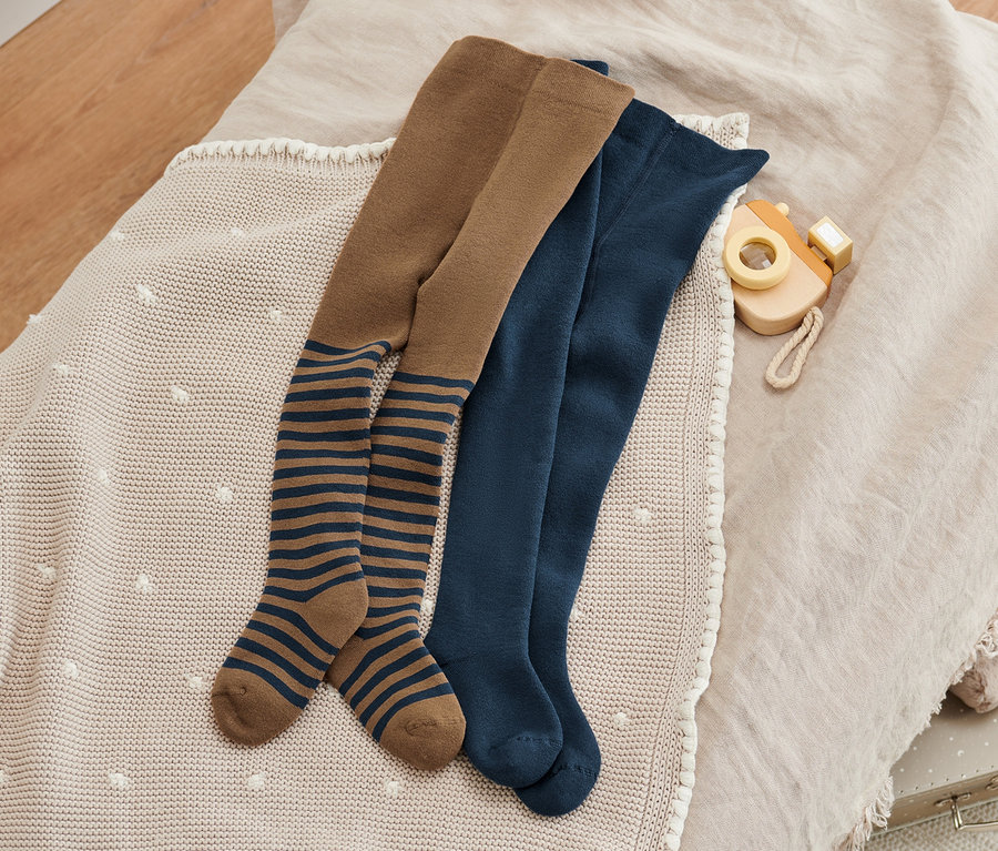 Zwei Paar Thermo-Strumpfhosen, blau und braun mit blauen Streifen, liegen auf einer Decke neben einem Spielzeug.