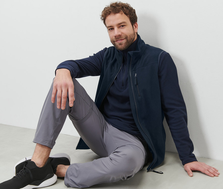 Mann sitzt am Boden und trägt eine Fleece-Weste.