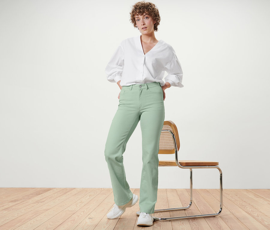 Frau posiert in mintgrünen Bootcut Jeans – Fit »Lou« und weißem Hemd.