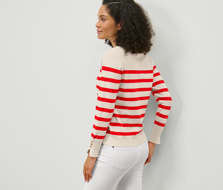 Seitenansicht einer Frau mit dunklen lockigen Haaren, die einen rot gestreiften Feinstrickpullover und weiße Jeans trägt.