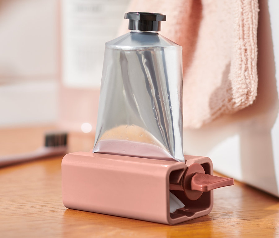 Silberne Tube in rosa Tubenpresser auf Holzkommode.