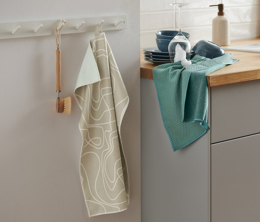 Zwei Geschirrtücher hängen in der Küche, eines beige mit Muster, das andere grün. 2 Geschirrtücher.