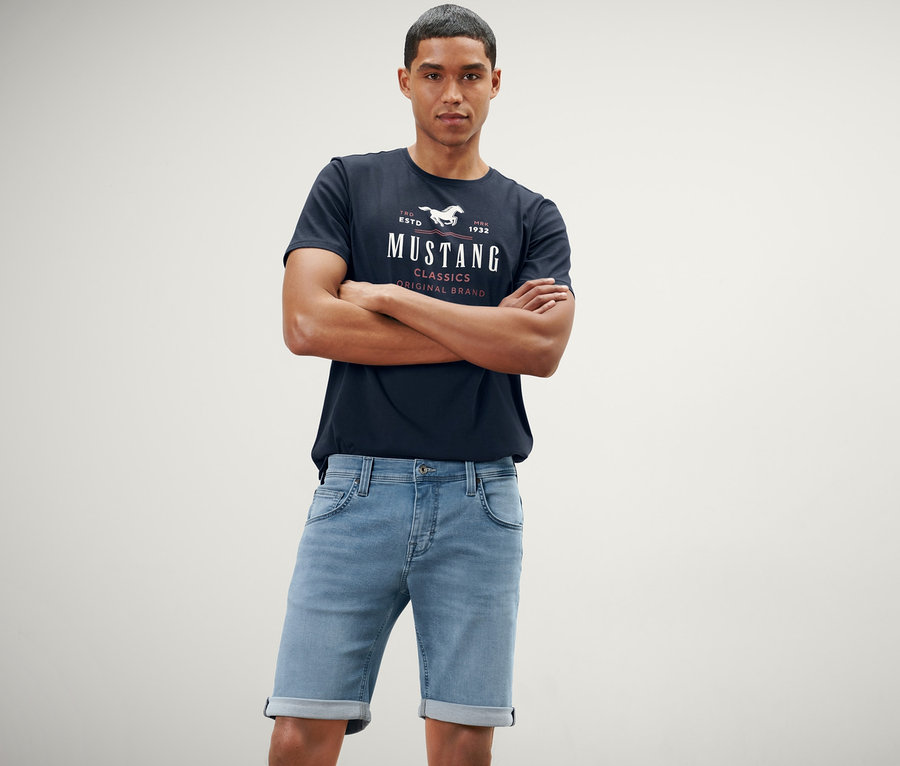 Mann posiert mit verschränkten Armen in hellblauen Jeans-Shorts »Mustang«.