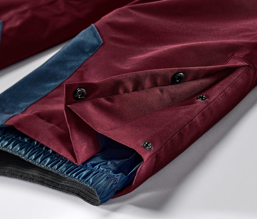 Detailaufnahme einer weinroten Ski-und-Snowboardhose mit blauen Akzenten und Knopfverschluss.
