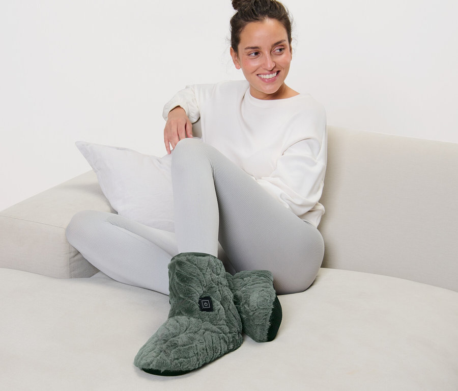 Frau sitzt auf Sofa und trägt beheizbare Schuhe.