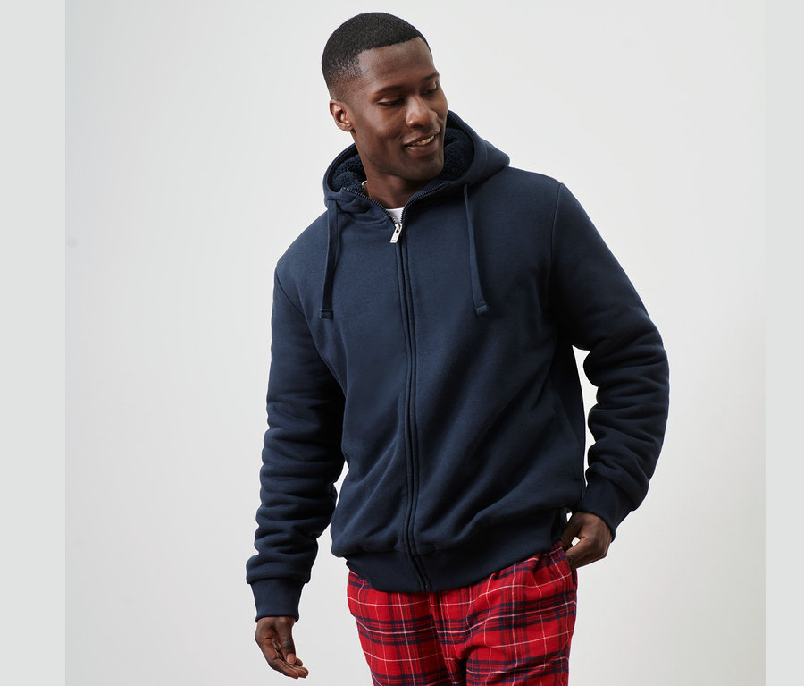 Mann trägt eine Kapuzen-Sweatjacke mit Teddyplüsch-Futter und karierte Hose.
