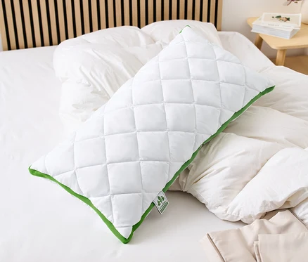 Ein weißes, gestepptes irisette® greenline Kopfkissen mit Klimaband und grüner Bordüre liegt auf einem Bett.