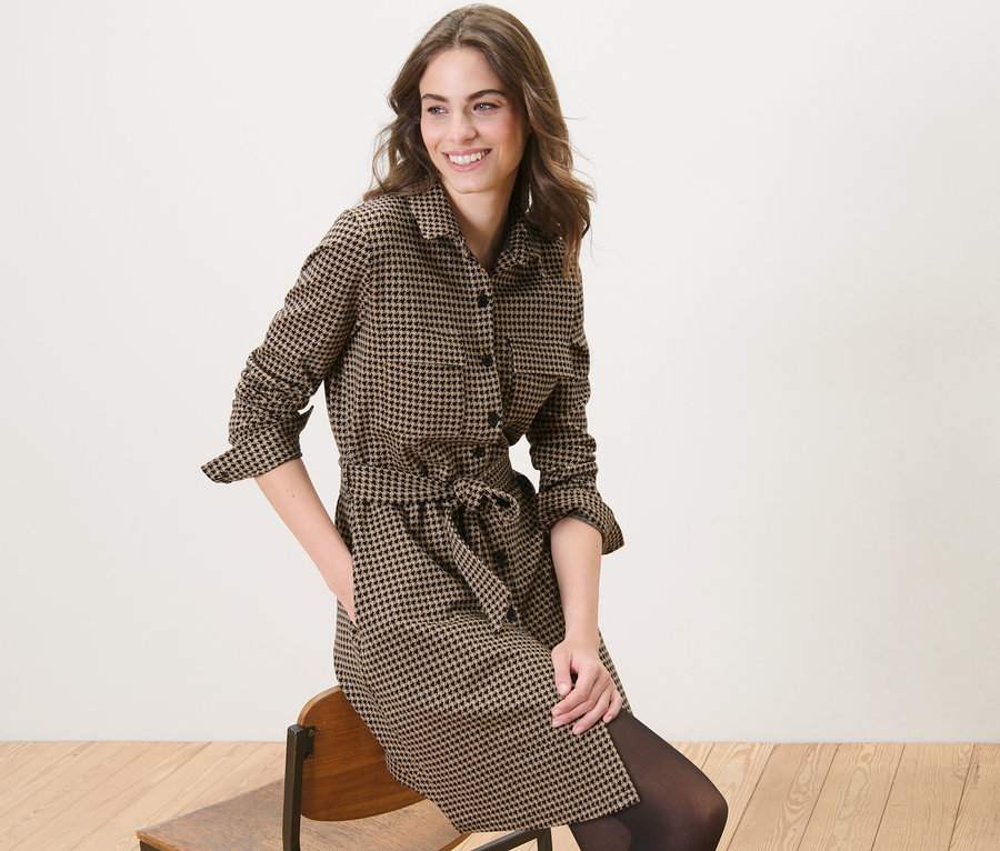 Frau sitzt auf einem Stuhl und trägt ein Sweatkleid mit Hahnentritt-Jacquard.