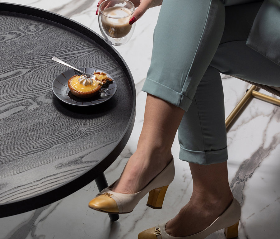 Frau hält Kaffee neben Woood Beistelltisch »Mesa XL«, Holz schwarz, darauf Teller mit Kuchen.