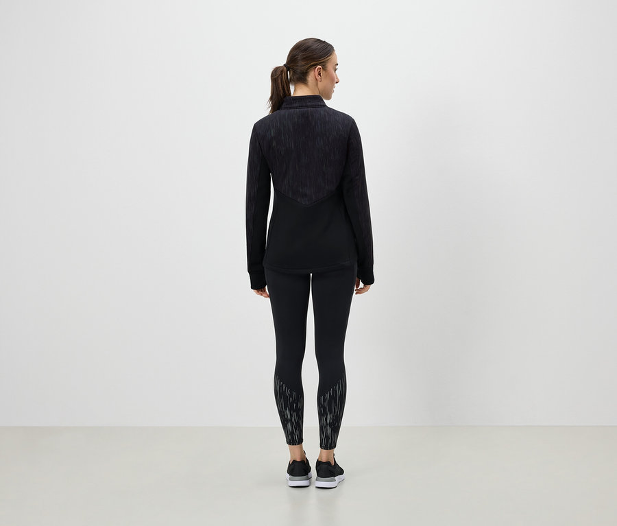 Frau steht mit dem Rücken zur Kamera und trägt schwarze Sportbekleidung.