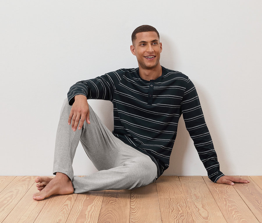 Mann sitzt im gestreiften Schlafanzugoberteil und grauer Hose am Boden.