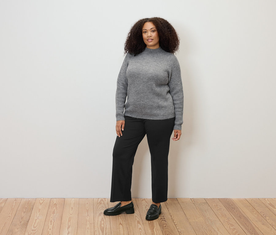 Frau steht und trägt einen grauen Grobstrickpullover mit Stehkragen und eine Komfort-Jerseyhose.