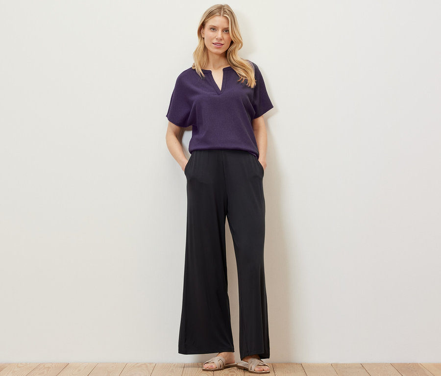 Blonde Frau posiert in strukturierter Kurzarmbluse und schwarzer Hose.