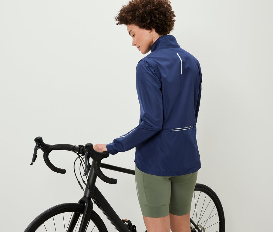 Frau steht mit einem Fahrrad und trägt eine 2-in-1-Fahrradjacke.