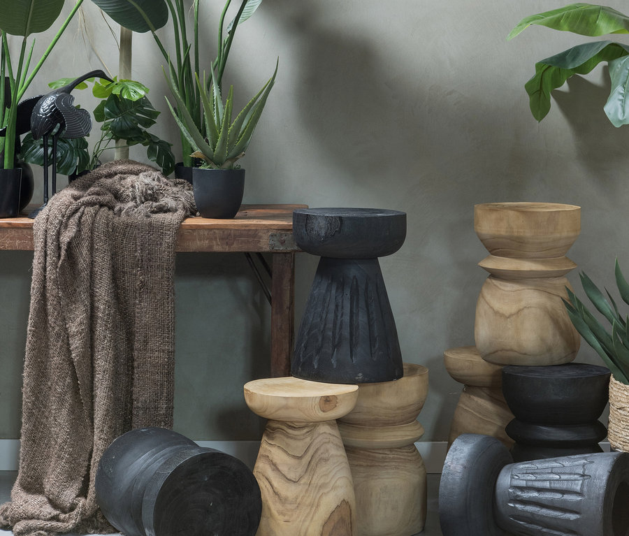 Verschiedene Woood Bink Hocker aus Holz in Naturfarbe und Schwarz sind in einem Raum mit Pflanzen arrangiert.