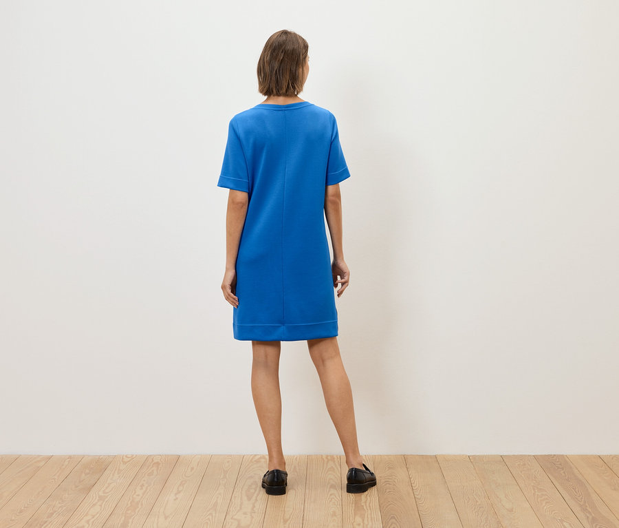 Frau mit dem Rücken zur Kamera trägt ein blaues Kleid und schwarze Schuhe.