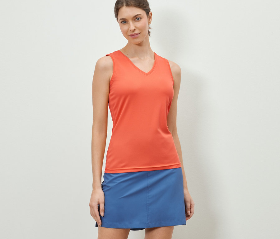 Eine Frau trägt ein orangefarbenes V-Neck-Funktionstop und einen blauen Rock.
