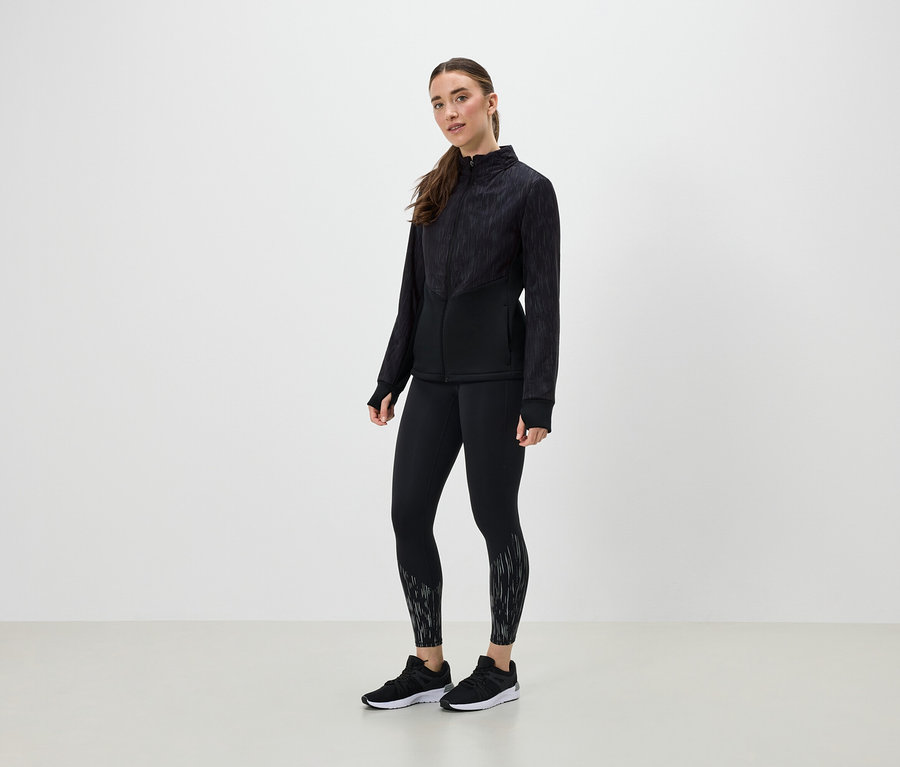 Eine Frau in schwarzer Sportbekleidung posiert vor einem hellen Hintergrund.