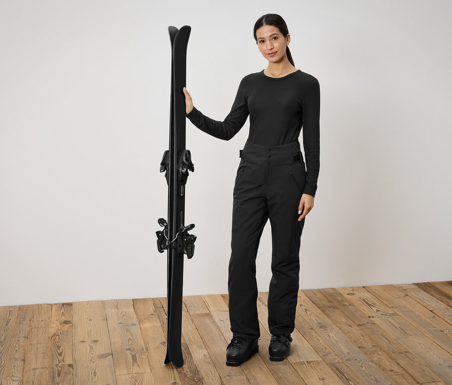 Frau in schwarzer Skibekleidung hält schwarze Ski.