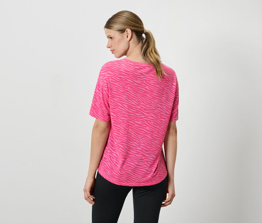 Eine Frau von hinten trägt ein pinkes Shirt mit Tiermuster und schwarze Hosen.