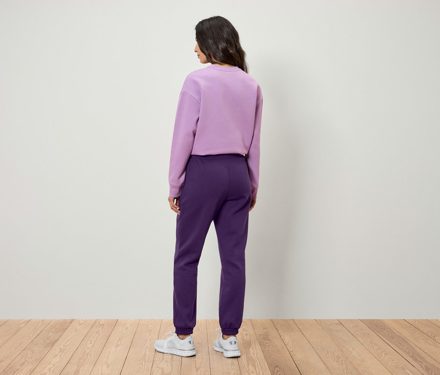 Frau mit dem Rücken zur Kamera trägt ein lila Sweatshirt und eine lila Jogginghose.