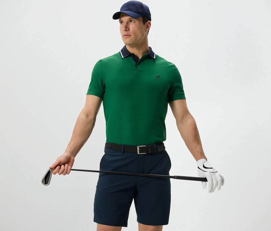 Mann hält Golfschläger und trägt ein grünes Funktions-Poloshirt.