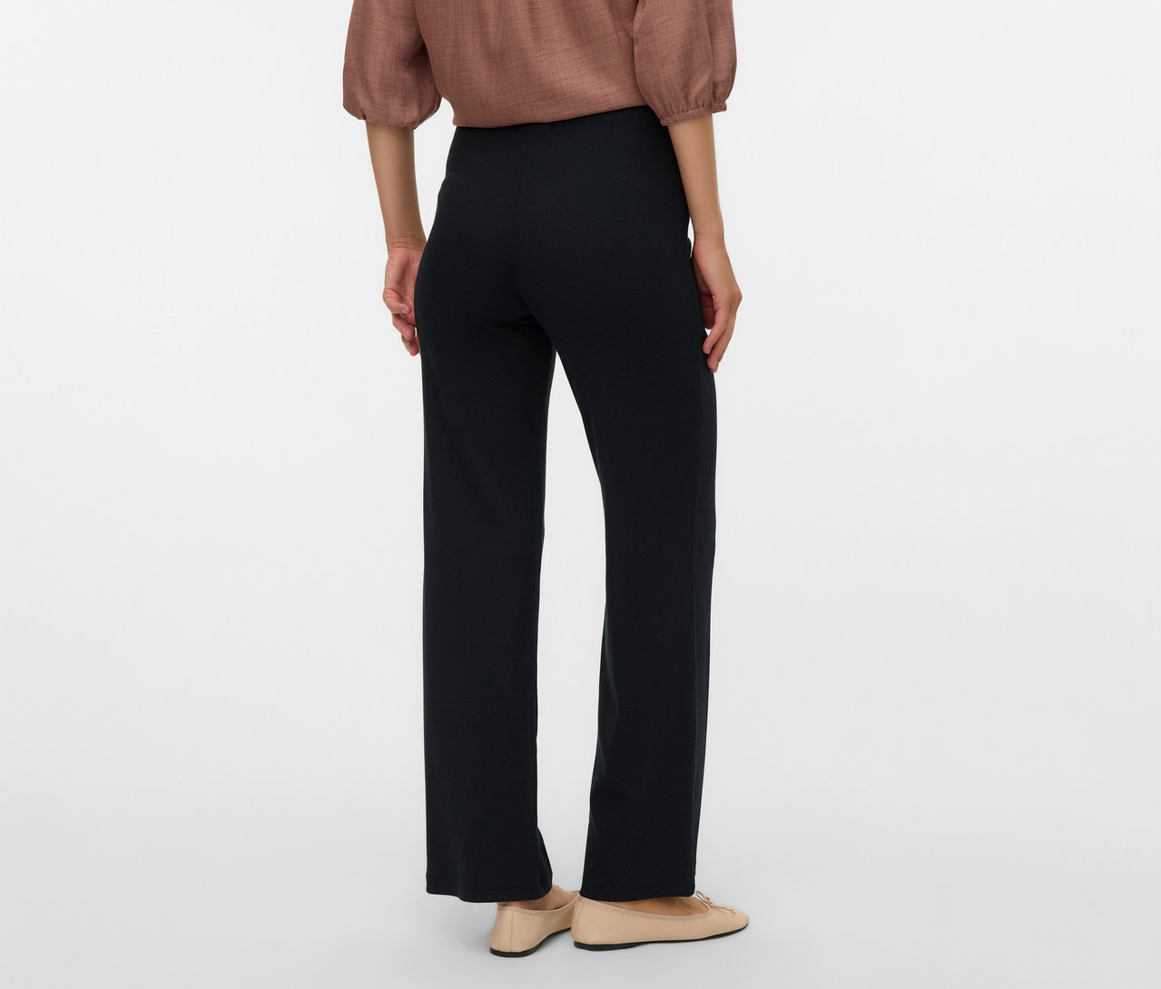 Rückansicht einer Frau mit brauner Bluse und MAMALICIOUS lockeren Leggins »MLEMILY« in Schwarz, dazu flache, beigefarbene Schuhe.