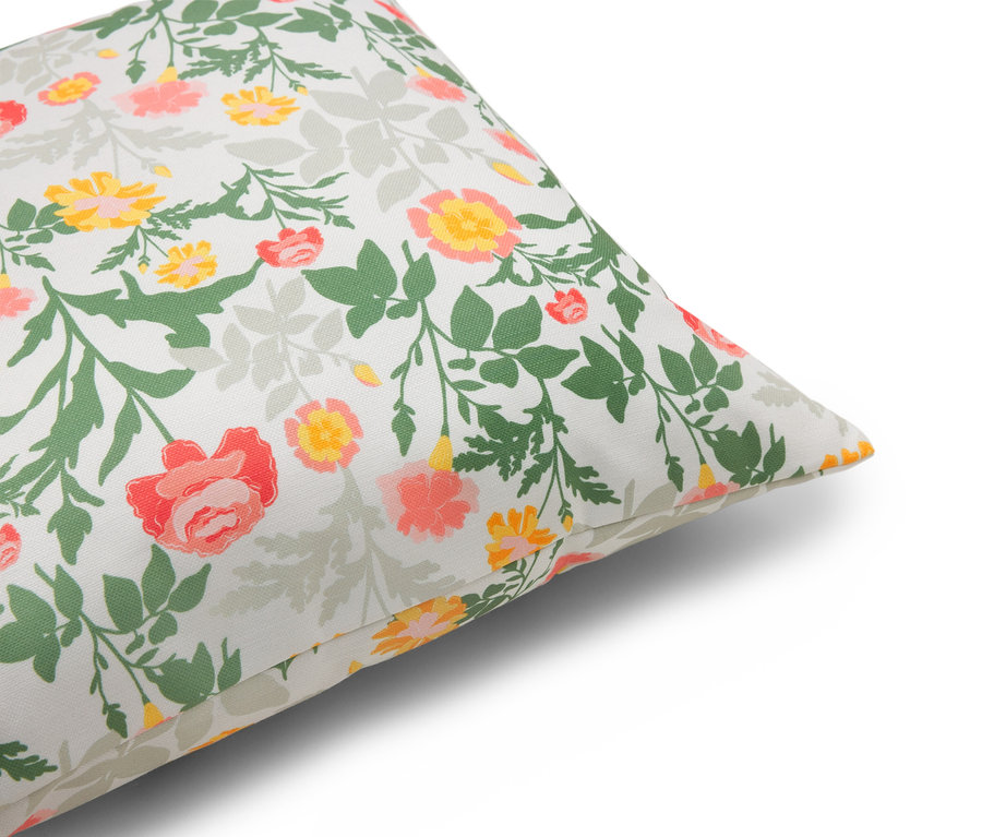 Nahaufnahme eines Kissens mit Blumenmuster in Rot-, Gelb- und Grüntönen auf weißem Grund.