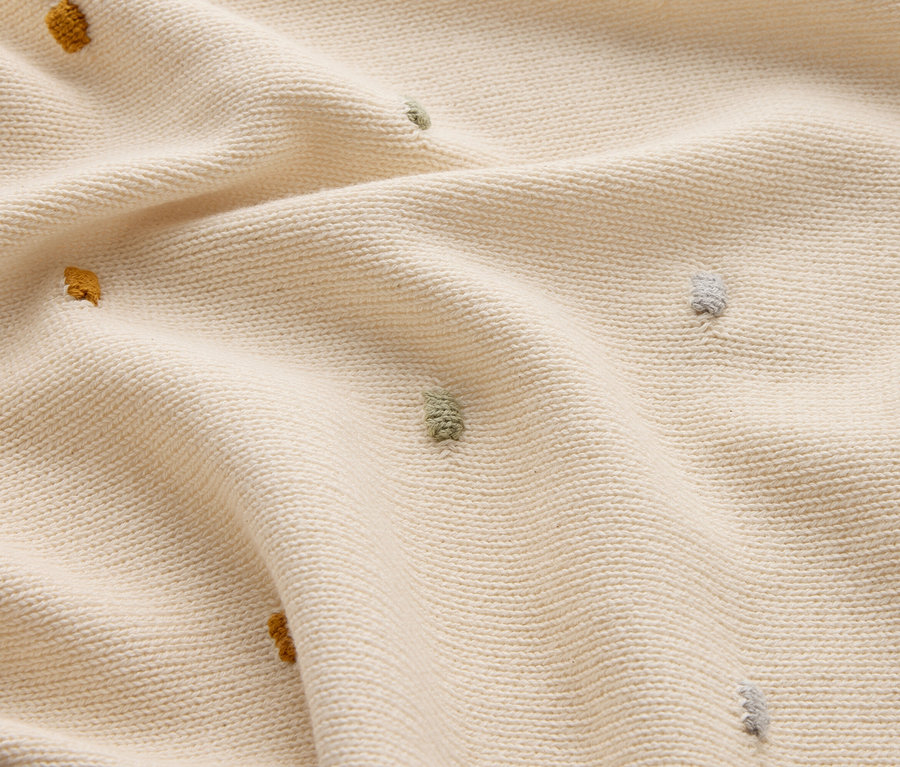 Nahaufnahme eines cremefarbenen Strickstoffs mit gelben, grünen und grauen Noppen.