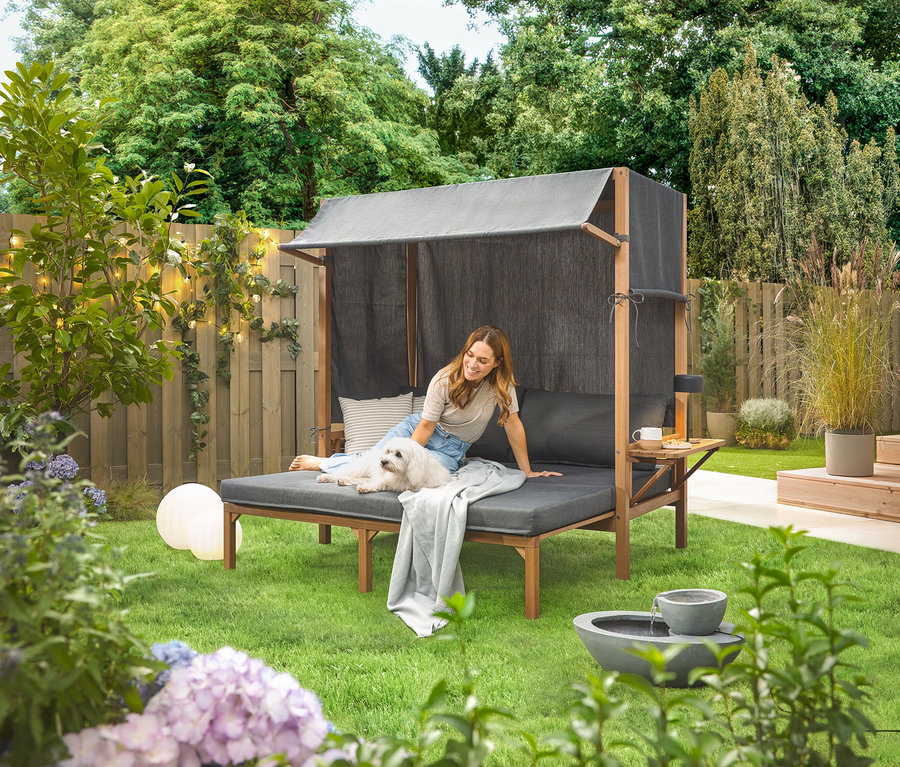 Frau sitzt mit Hund auf einem Solar-Gartenbrunnen im Garten.
