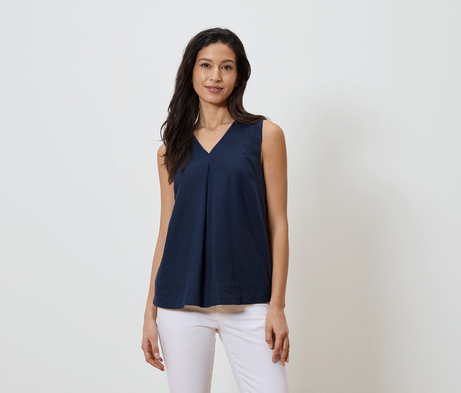 Frau trägt ein marineblaues, ärmelloses V-Ausschnitt-Top und weiße Jeans.