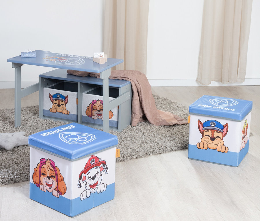 Ein blau-grauer Kindertisch mit zwei darunter liegenden Aufbewahrungsboxen und zwei Paw Patrol Aufbewahrungshockern auf einem Teppich.