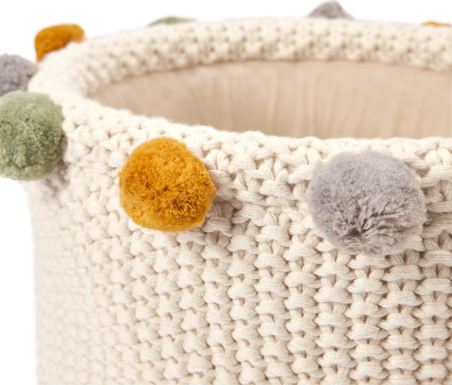 Nahaufnahme eines weißen, gestrickten Korbs mit farbigen Bommeln am Rand.