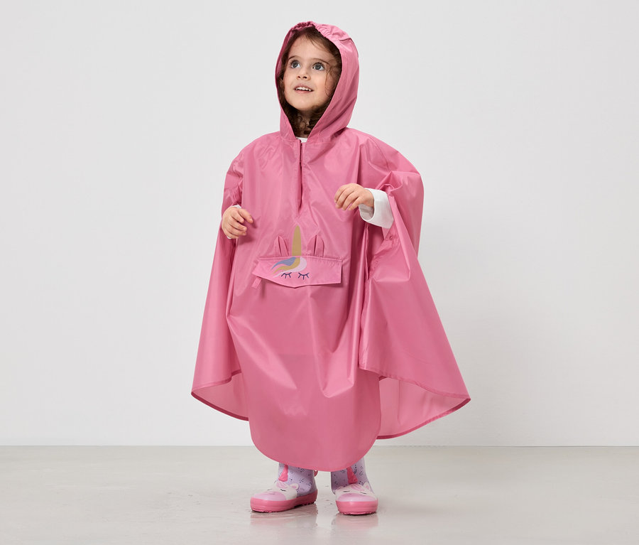 Ein kleines Mädchen trägt einen pinkfarbenen Regenponcho mit Kapuze und Einhorn-Motiv über ihrer Kleidung.