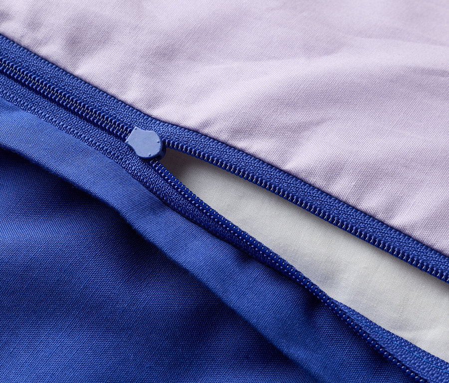 Nahaufnahme eines teilweise geöffneten Reißverschlusses an einem lilafarbenen und blauen Stoff.