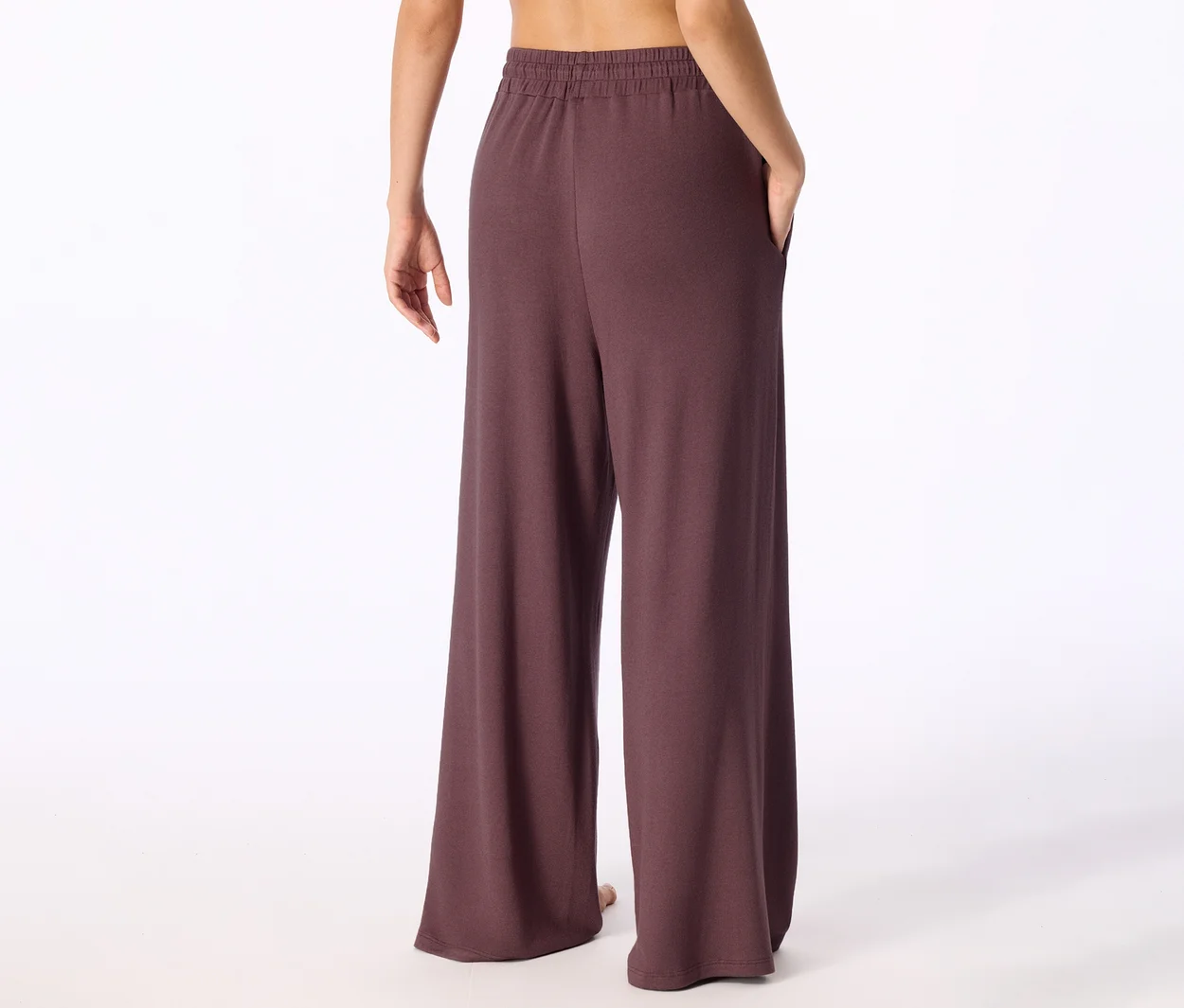 Person von hinten in weiten, dunkelbraunen Hosen mit Gummibund und einer Hand in der Tasche, der obere Rücken ist sichtbar.