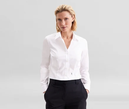 Blonde Frau in weißer Seidensticker Bluse Slim Fit non iron und dunkler Hose, Hände in den Taschen.