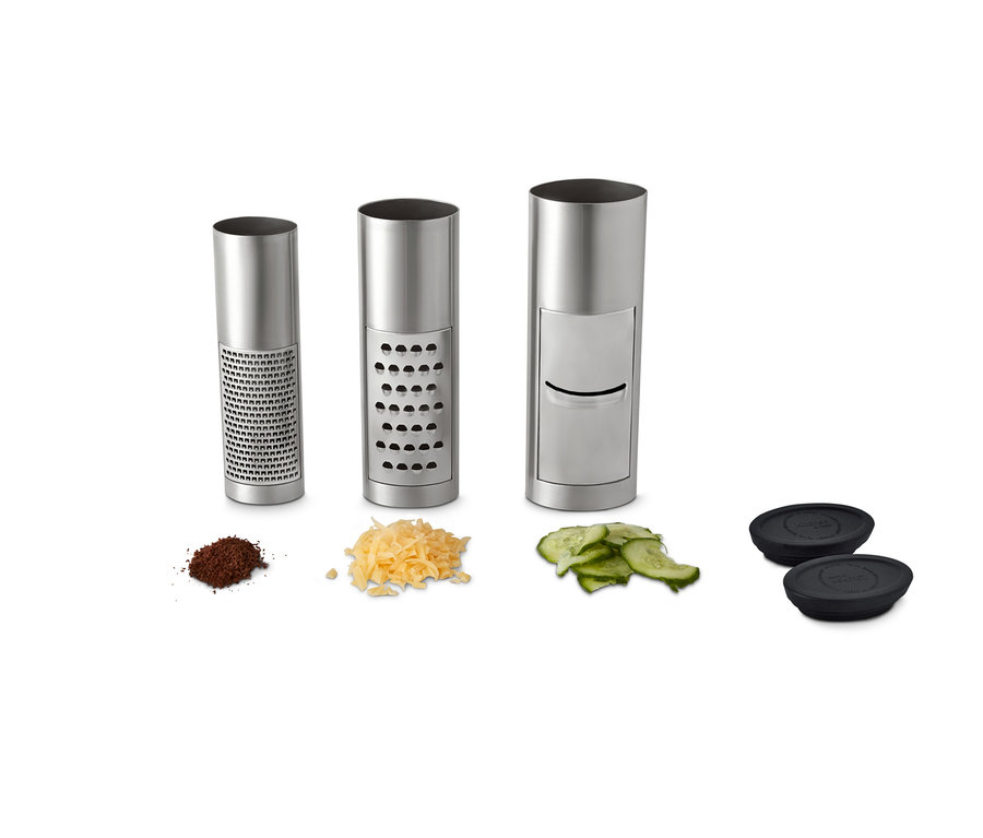 Reiben-Set: Drei silberne, zylindrische Reiben, drei Haufen geriebener Lebensmittel und zwei schwarze Deckel.