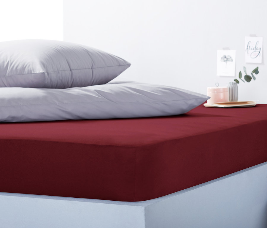 Ein rotes Jersey-Spannbettlaken, Doppelgröße, liegt auf einem Bett mit grauen Kissen.